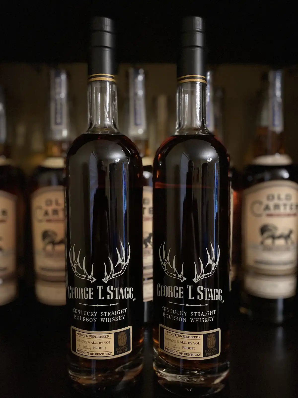 Two identical bottles of George T. Stagg Kentucky Straight Bourbon Whiskey stand side-by-side, their labels featuring a…