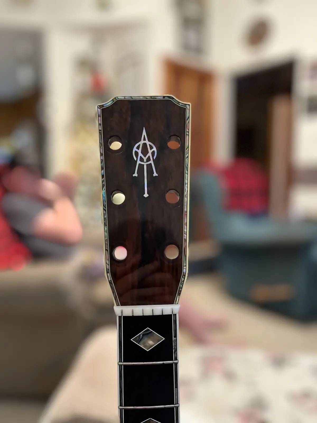 A close-up photo shows the headstock of a dark wood guitar with a silver inlaid symbol resembling a satanic sigil at its…