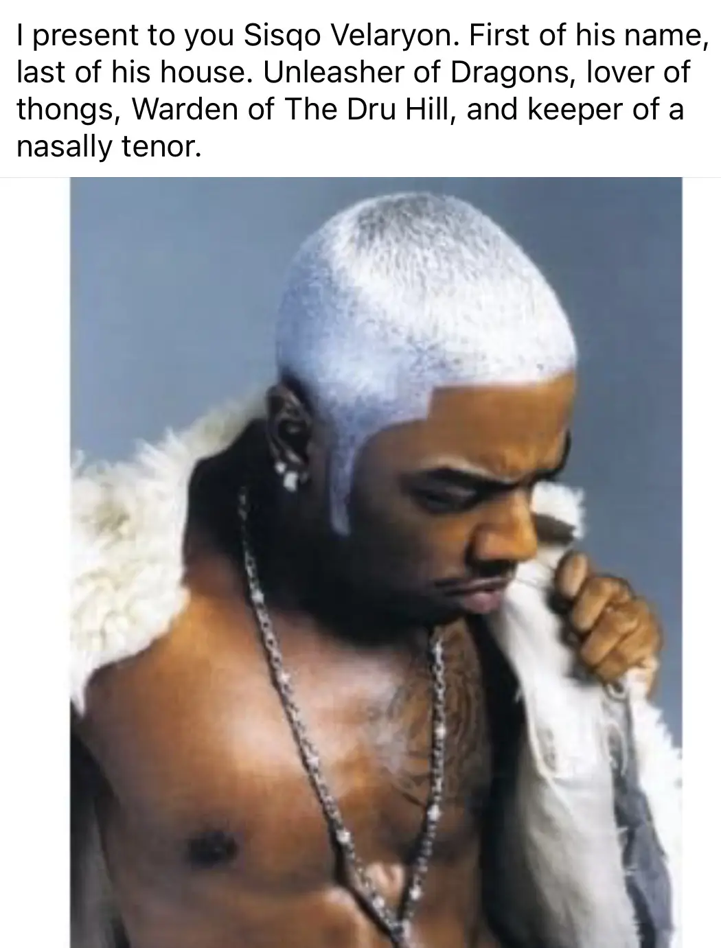 A shirtless man with a shaved, bleached blonde head and dark skin, wearing a white fur-trimmed jacket and a silver chain…