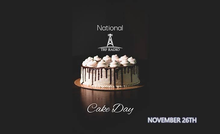 A professionally lit, round cake with white frosting and chocolate drizzle sits on a reflective surface against a dark…