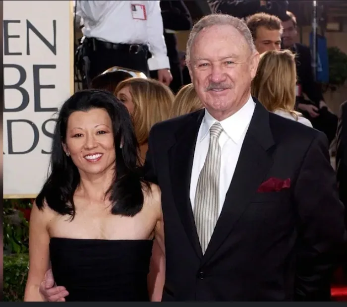 A man and woman pose together on a red carpet in front of a 'GOLDEN GLOBES' sign. The man, wearing a black suit with a…