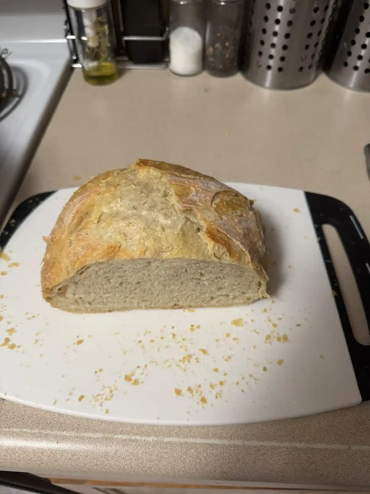 A loaf of homemade bread sits on a white cutting board with black handles, half-sliced to reveal its interior. Crumbs are…