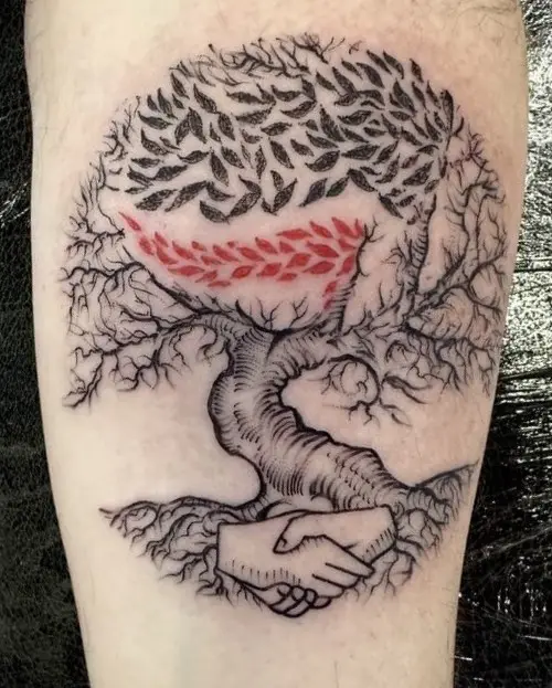 A black-and-white tattoo on a leg depicts a stylized tree with intricate roots and branches, where the roots form a…