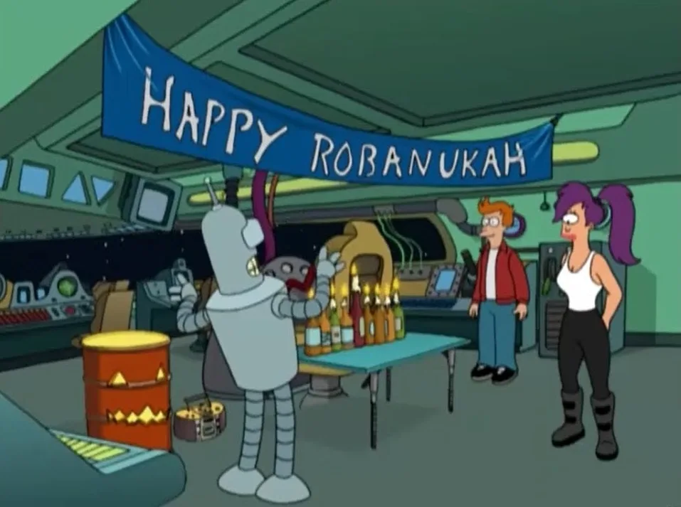 In a cartoon spaceship interior, a robot stands at a table with bottles and lit candles, under a blue banner reading 'HAPPY…