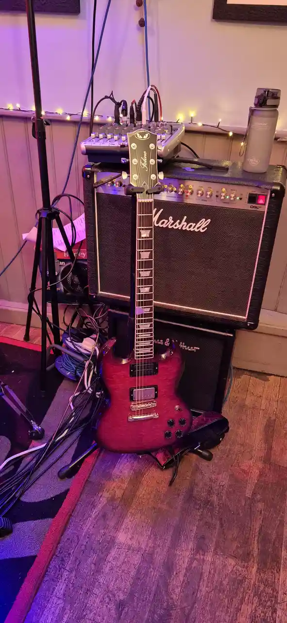 A red electric guitar with a 'Jeline' headstock is propped upright against a Marshall DSL40 amplifier, surrounded by tangled…