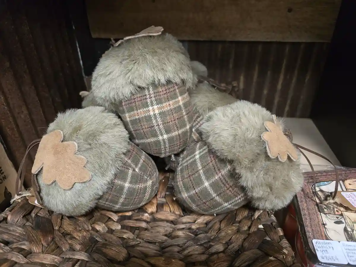 Three plush, fuzzy acorn-shaped decorations with plaid fabric bodies and felt leaf accents sit in a woven basket. The…