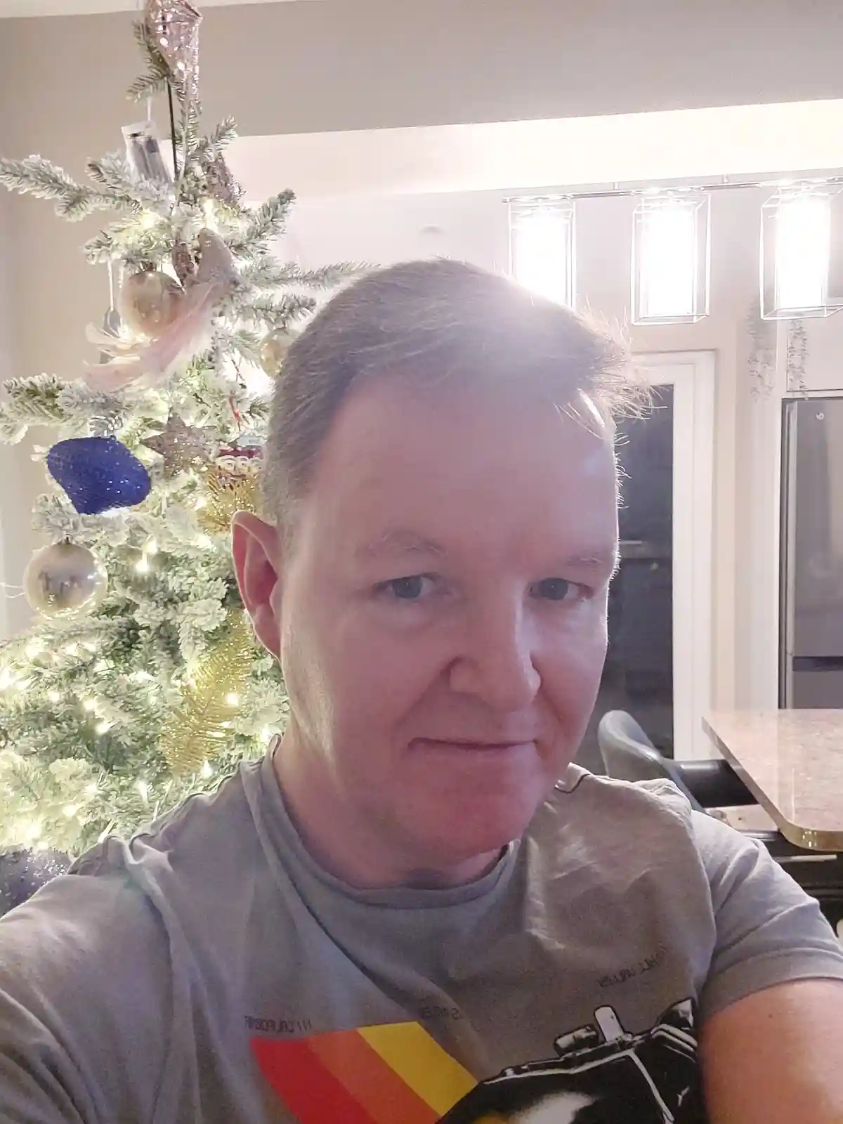 A man with gray hair and a gray t-shirt looks directly at the camera with a slightly annoyed or unimpressed expression…