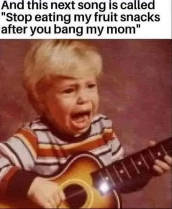 A young child with blonde hair, wearing a striped shirt, is visibly crying while holding a small acoustic guitar. The…