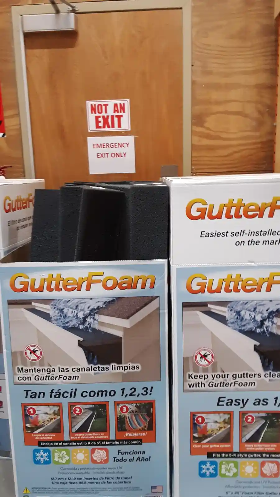 A photo shows boxes of GutterFoam gutter cleaning inserts in a store aisle, with a wooden door behind them bearing two…