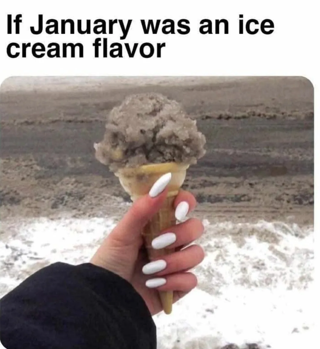 A hand with white nail polish holds an ice cream cone whose scoop is covered in dirty, grayish snow, set against a snowy…