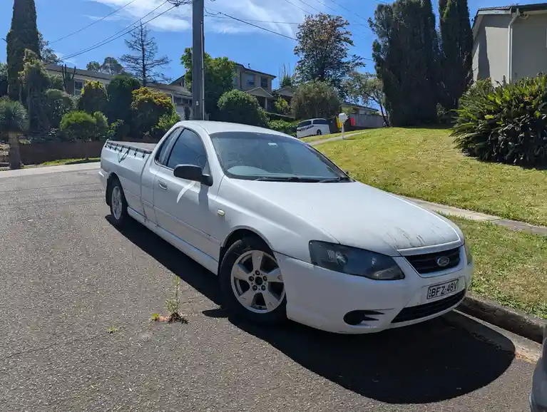 A white Ford pickup truck, specifically a utility model, is parked on a residential street under a clear blue sky. The…