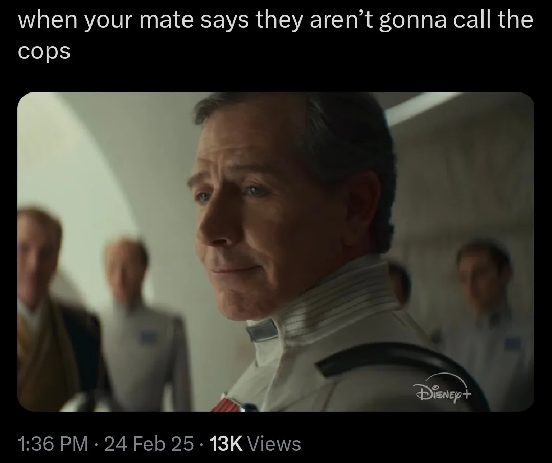 A still image from a Disney+ show features a man in a white uniform with a subtle, knowing smirk, looking off to the side…