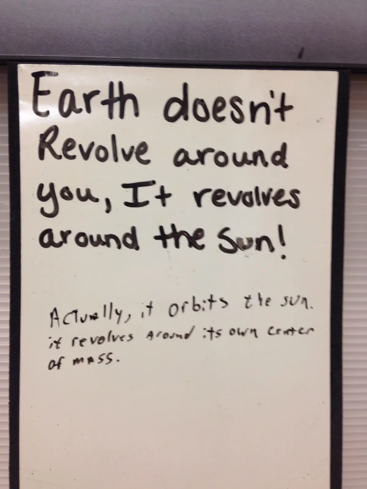 A handwritten note on a whiteboard with black marker text, stating 'Earth doesn't Revolve around you, It revolves around the…