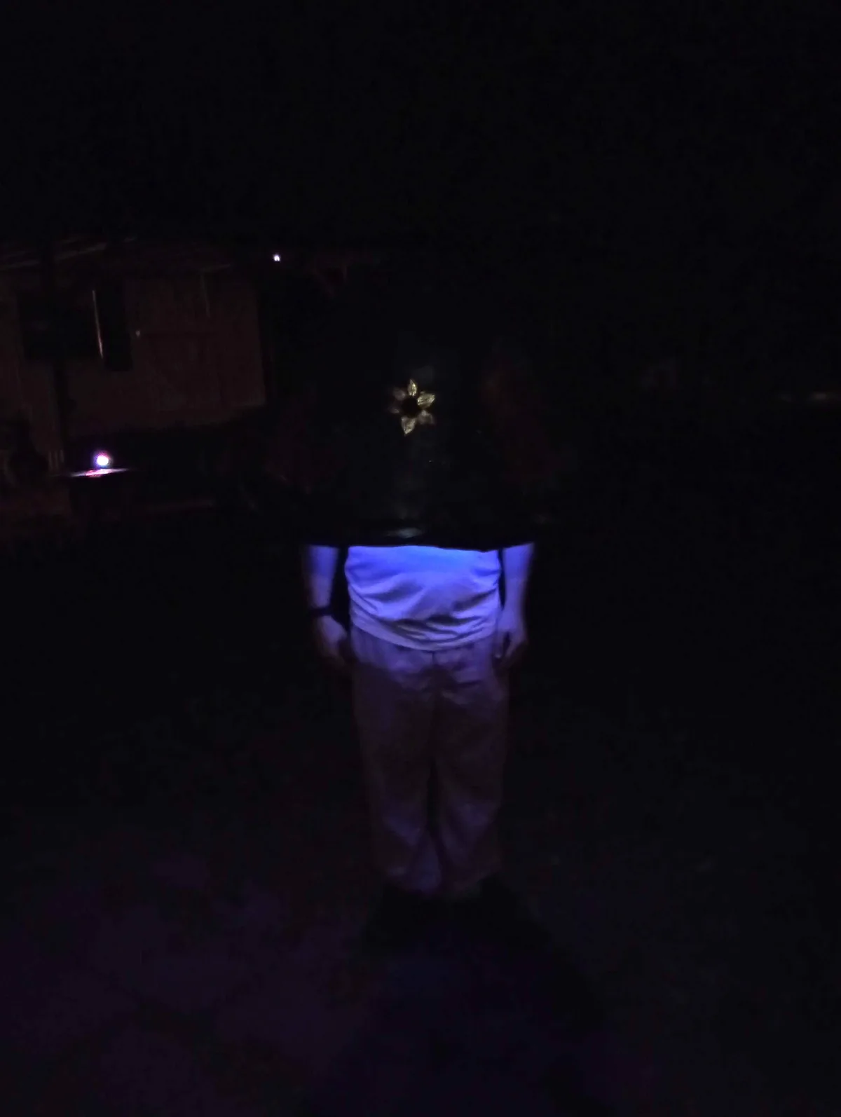 A person stands in near-total darkness, viewed from behind, wearing a backpack with a glowing blue light emanating from the…
