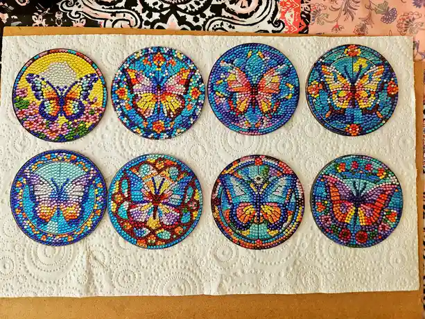 Eight circular coasters, each decorated with a colorful butterfly design made from tiny beads, are arranged in two rows on a…