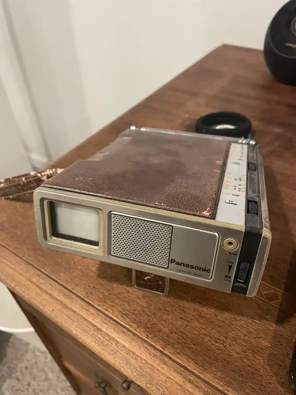 A vintage Panasonic TV/FM-AM radio with a brown textured cover and silver casing sits on a wooden surface, showing signs of…