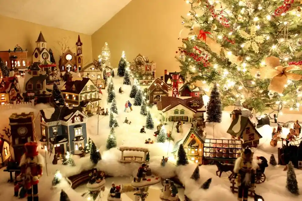 a lavish, illuminated christmas village diorama with miniature houses, trees, and figurines arranged on a snowy slope…