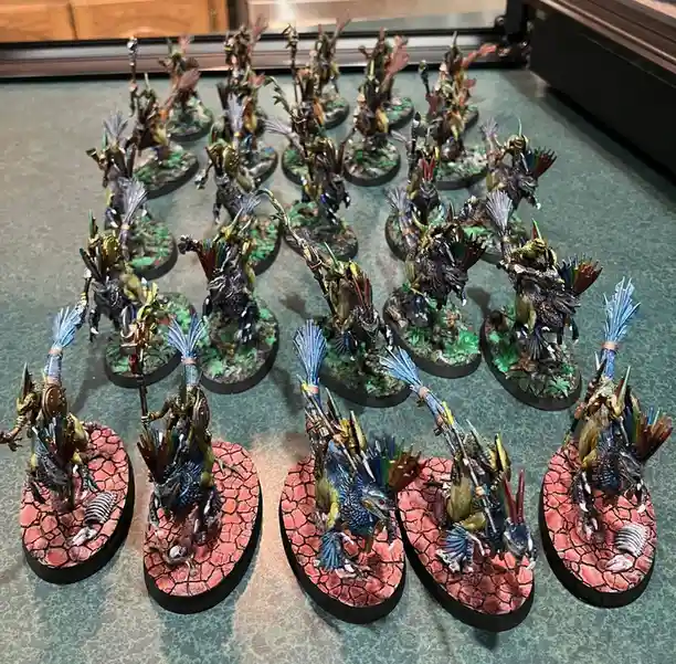 A collection of intricately painted fantasy miniatures, likely for tabletop wargaming, arranged in rows on a green surface…