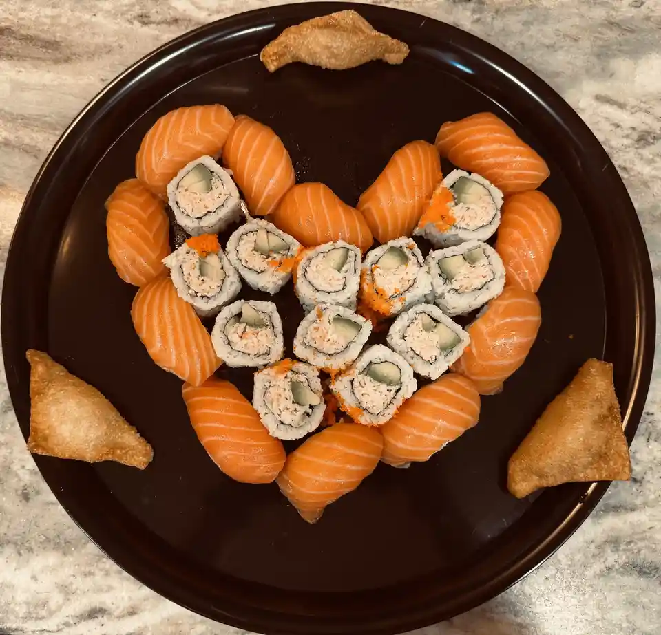 A top-down photo of a black plate holding sushi arranged to form a heart shape, with salmon nigiri forming the outer curve…