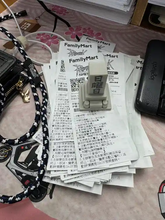 A pile of FamilyMart receipts is topped by a white plastic toy resembling a Japanese 'Sunday' (日曜日) character, surrounded by…