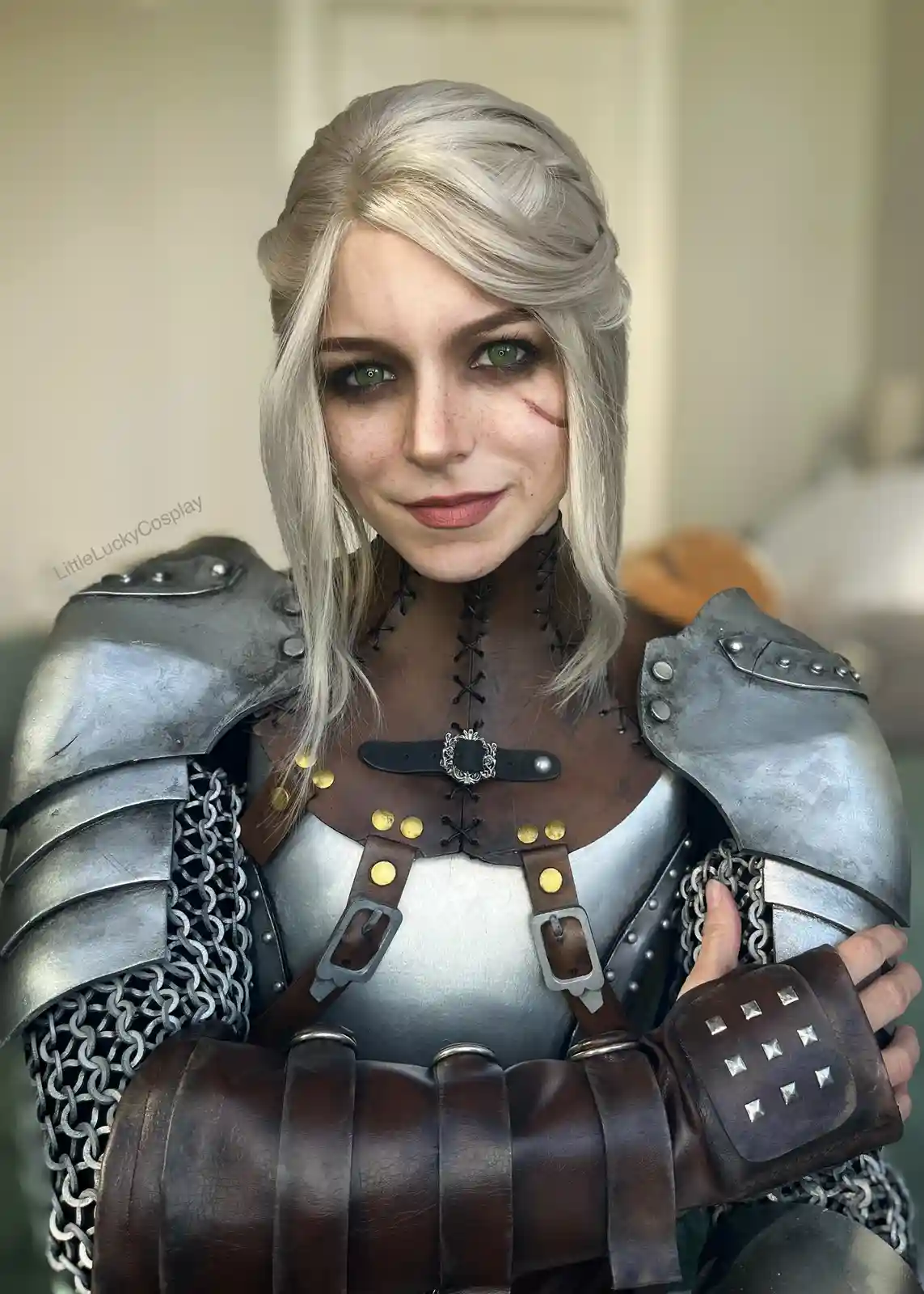 A person in detailed cosplay as a fantasy warrior, wearing silver armor, chainmail, and brown leather bracers with metal…