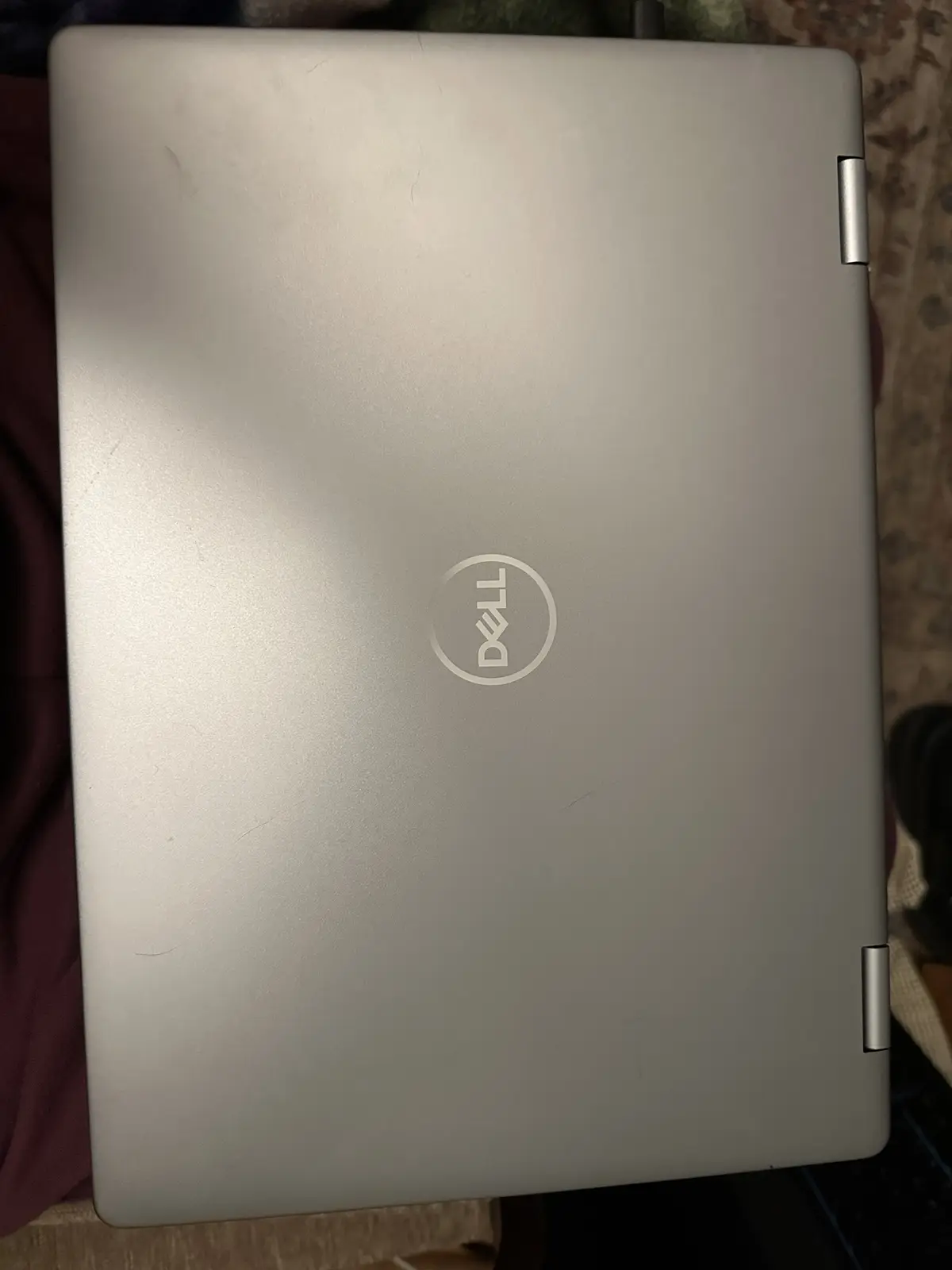 A silver Dell laptop with a visible logo on its closed lid, showing minor scratches and scuffs, resting on a patterned…