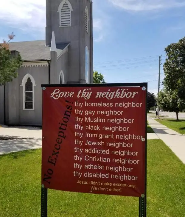 A red sign in front of a church lists 'Love thy neighbor' followed by specific groups like 'homeless neighbor', 'gay…
