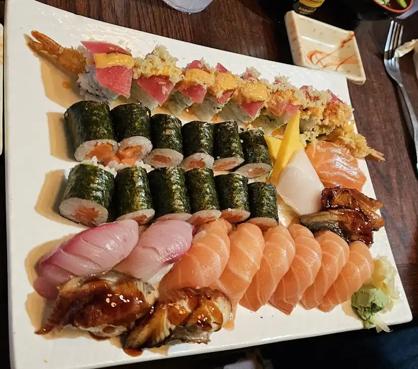 a large white rectangular plate is filled with an assortment of sushi including tempura rolls, maki rolls wrapped in…