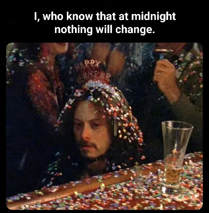A man with a 'Happy New Year' tiara and confetti on his head and shoulders sits at a bar covered in confetti, looking…