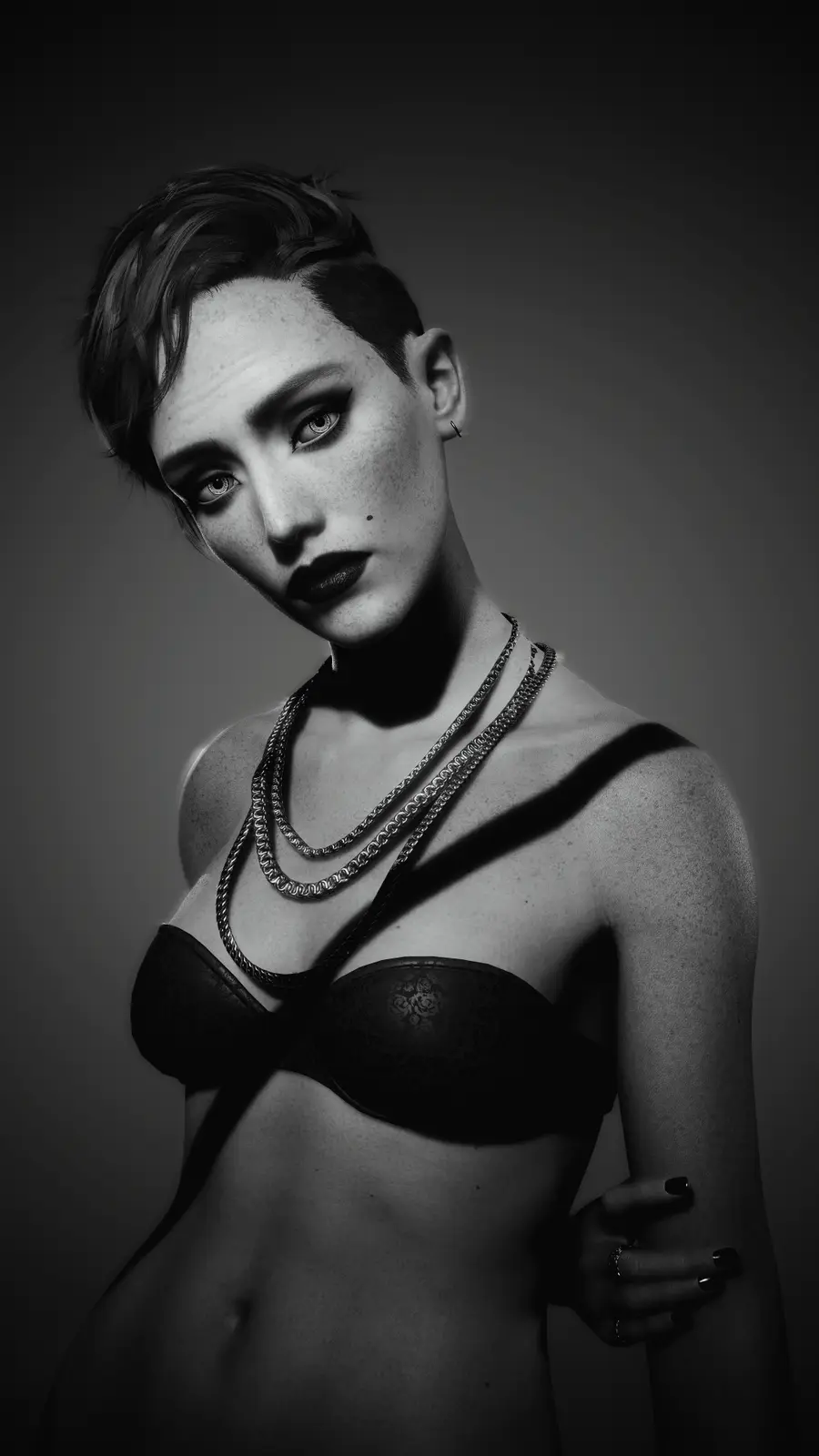 A black-and-white portrait of a woman with short hair, freckles, and dark lipstick, wearing a black bra and layered chains…