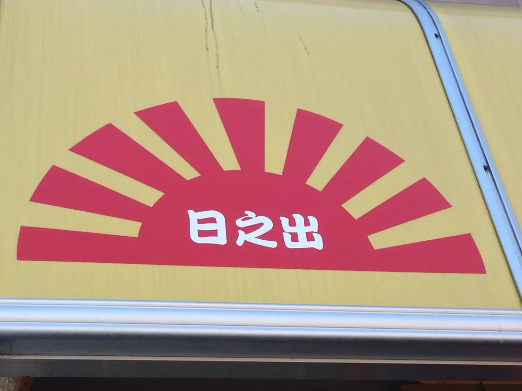 A close-up of a yellow surface with a red rising sun emblem and white Japanese characters '日之出' centered beneath it…