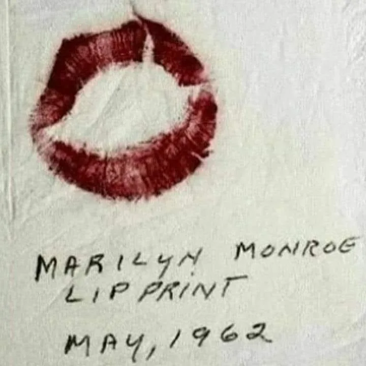 A close-up photograph shows a red lipstick mark on textured white paper, resembling a kiss. Below the mark, handwritten text…