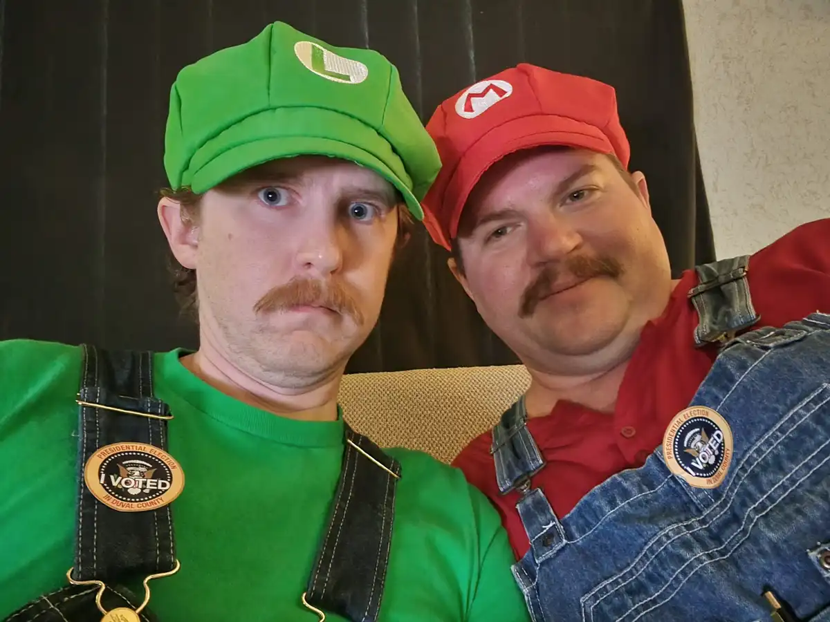 Two men dressed as Mario and Luigi, both wearing 'I Voted' presidential election pins, sit side by side. The man as Luigi…