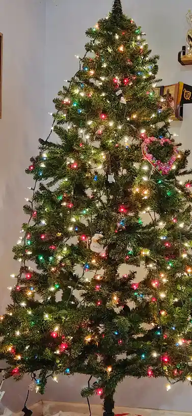 A decorated artificial Christmas tree with multicolored string lights and various ornaments, including a snowman and a pink…