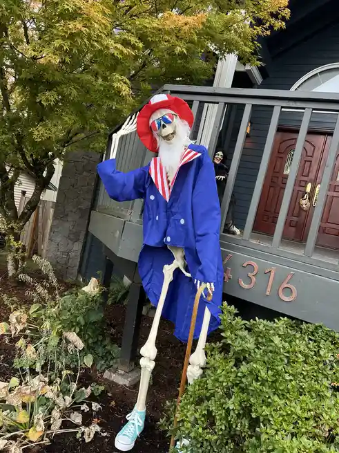A skeleton Halloween decoration dressed in a blue sailor suit with red and white stripes, wearing a red hat, sunglasses with…