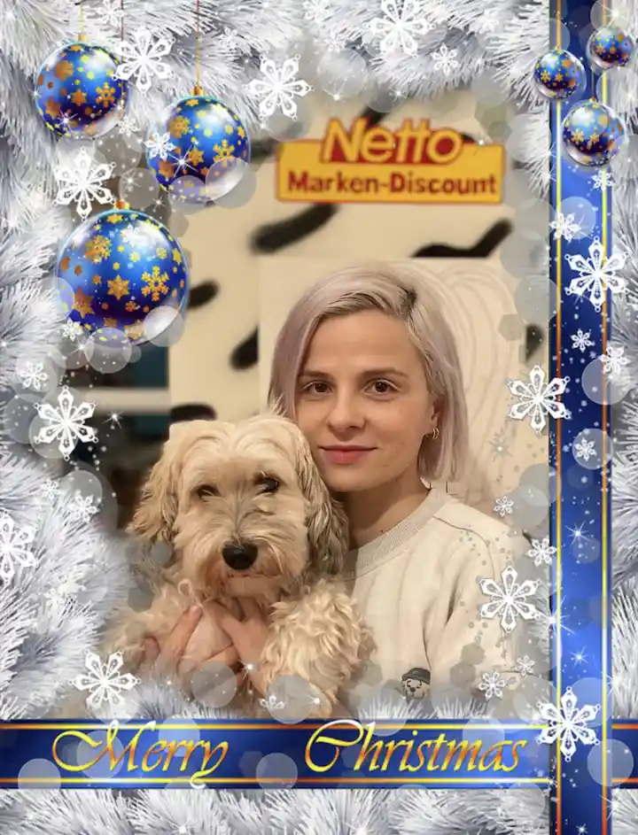 A person with short light-colored hair holds a fluffy light-brown dog in front of a 'Netto Marken-Discount' store sign. The…
