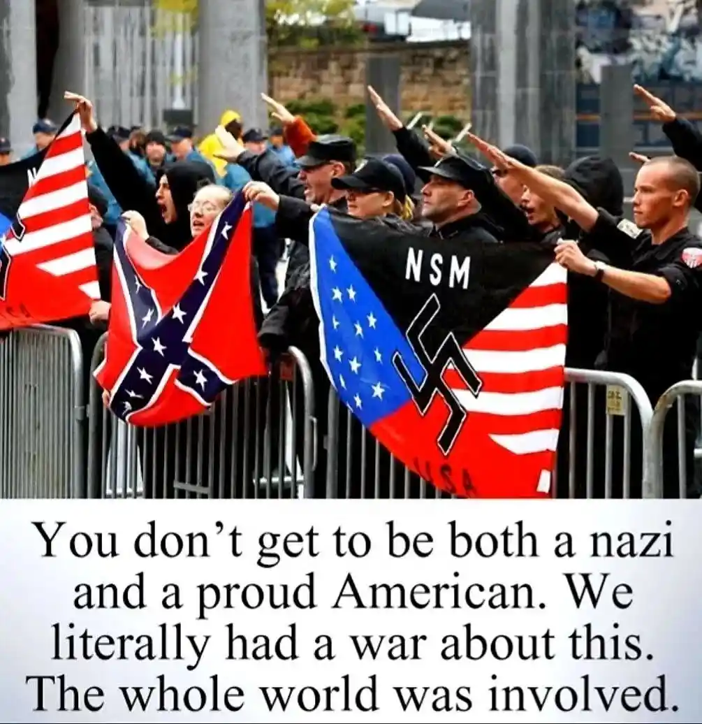 A group of people, some in uniform, stand behind metal barricades outdoors, raising their right arms in a Nazi salute while…