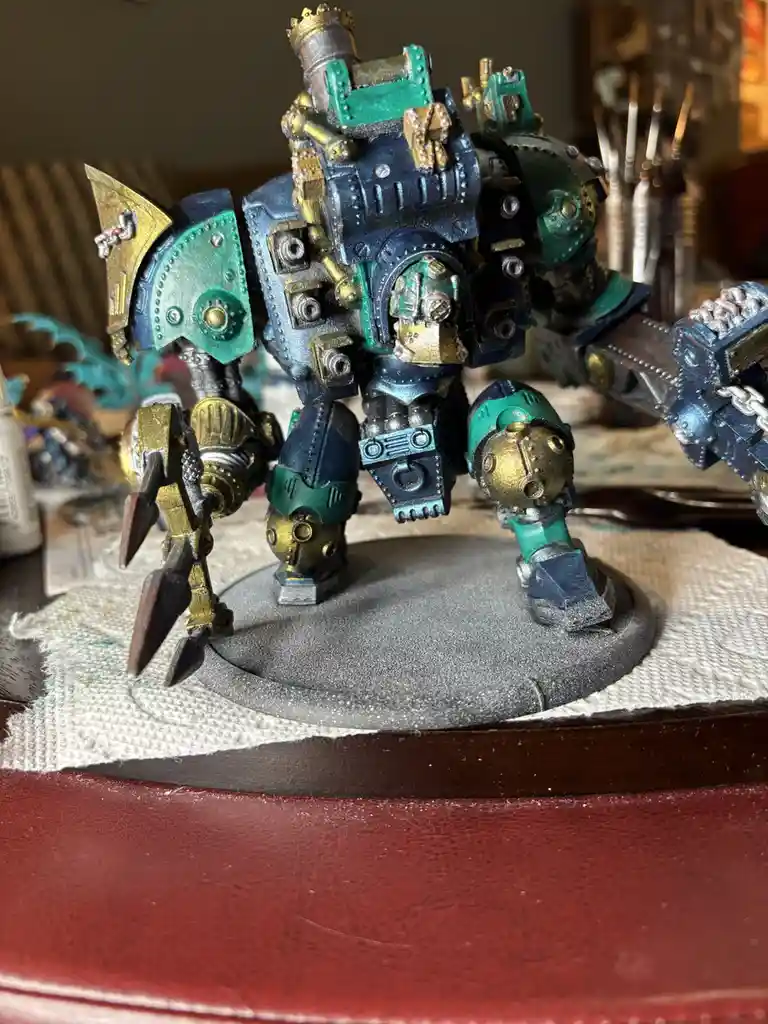A heavily detailed, custom-painted miniature of a large, armored, biomechanical warrior with teal, blue, and gold coloring…