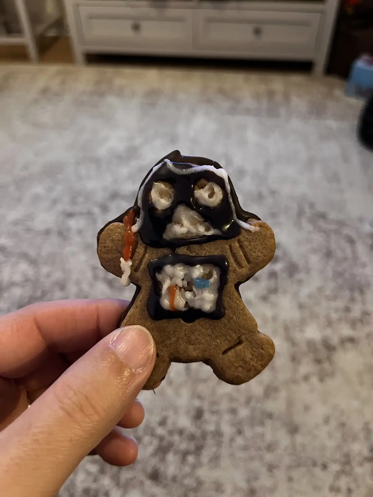 A hand holds up a gingerbread man cookie decorated with chocolate icing that drips down its face and torso, revealing a…