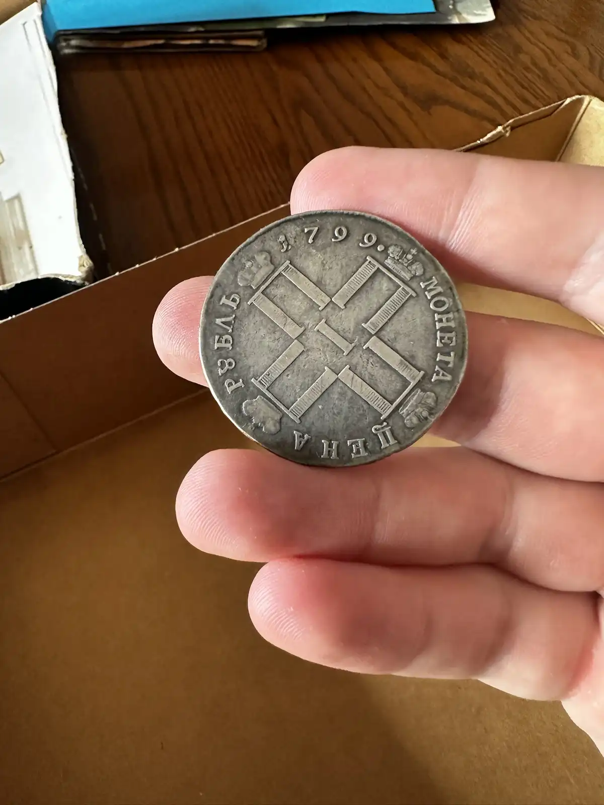 A hand holds an old silver coin dated 1799, with Cyrillic text reading 'РУБЛЬ 1799. МОНЕТА ЦЕНА' and a cross-like design…