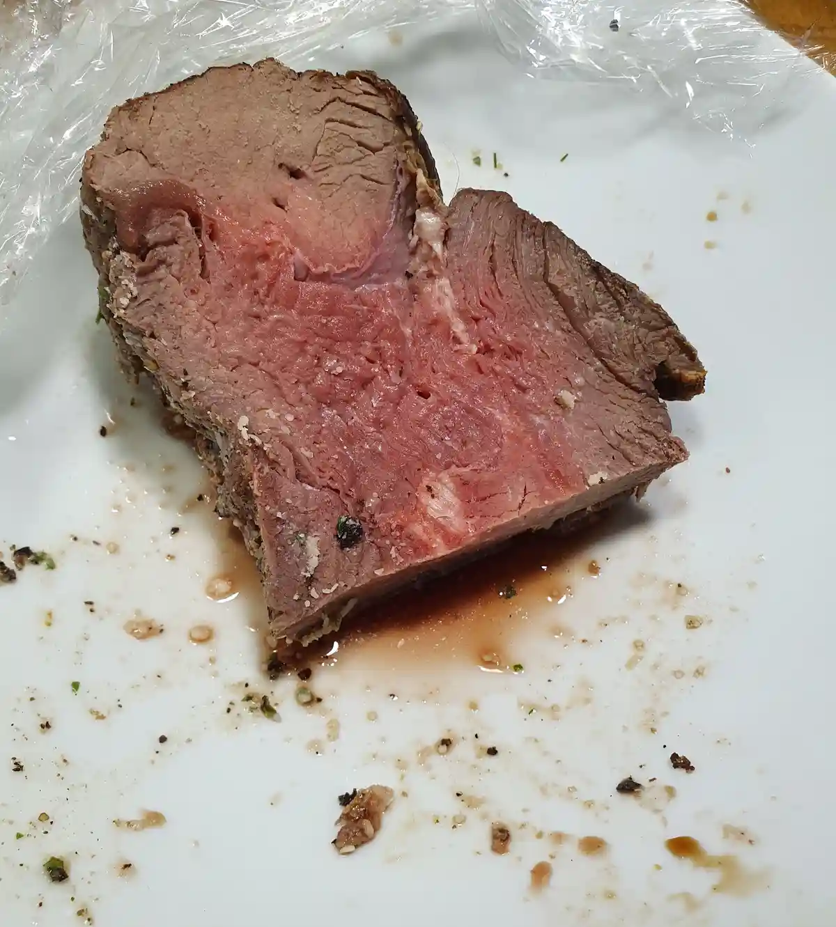 A close-up photo shows a slice of cooked roast beef on a white plate, revealing a pink, medium-rare interior and a browned…