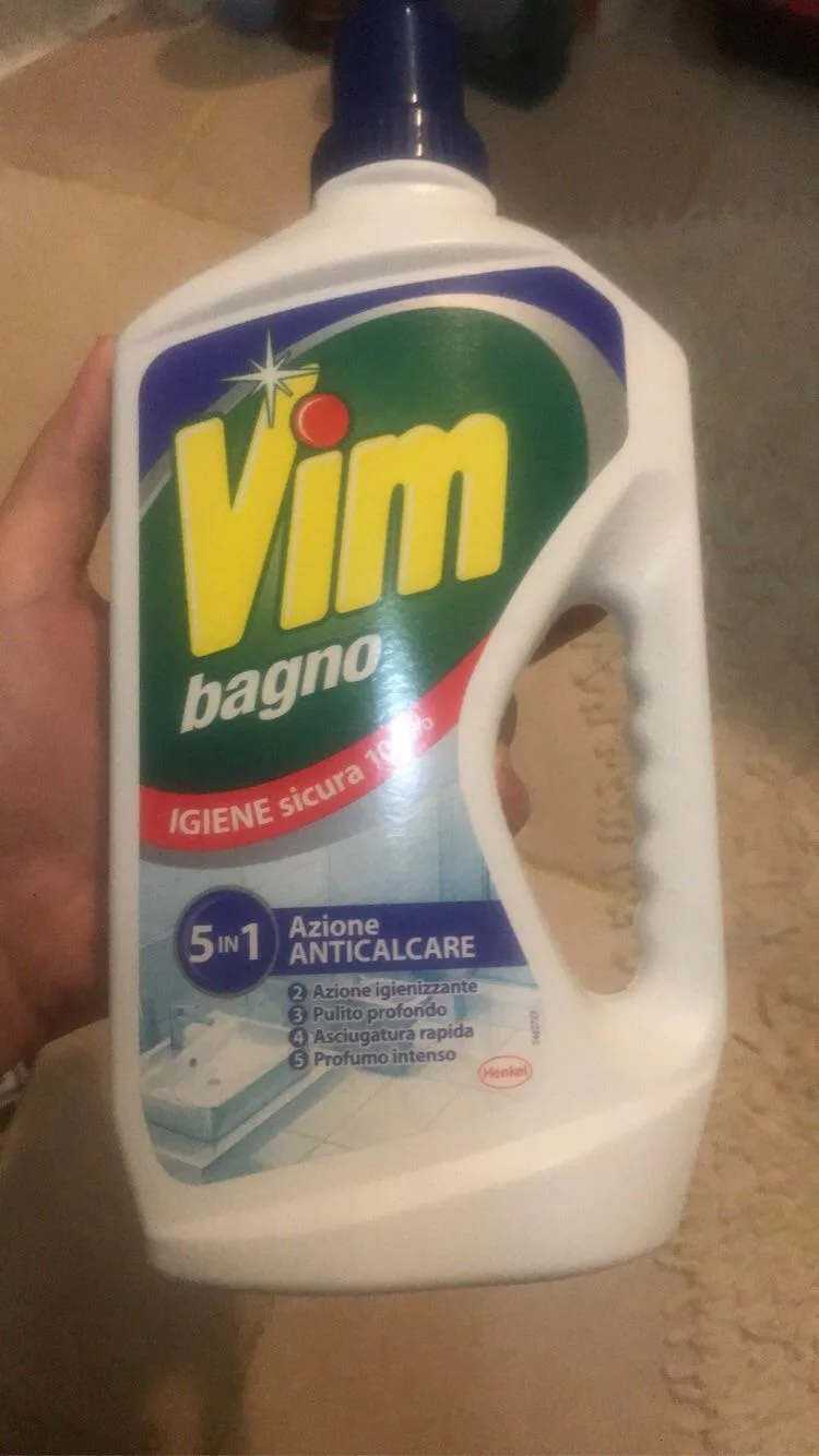 A hand holds a white plastic bottle of Vim bagno bathroom cleaner, featuring a green and yellow logo with Italian text…