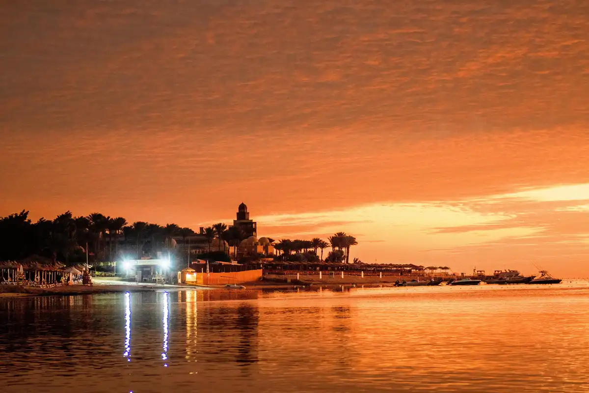 A serene beach scene at sunset or sunrise with an orange sky reflected in calm water, featuring a lit 'DIVING CENTER' sign…