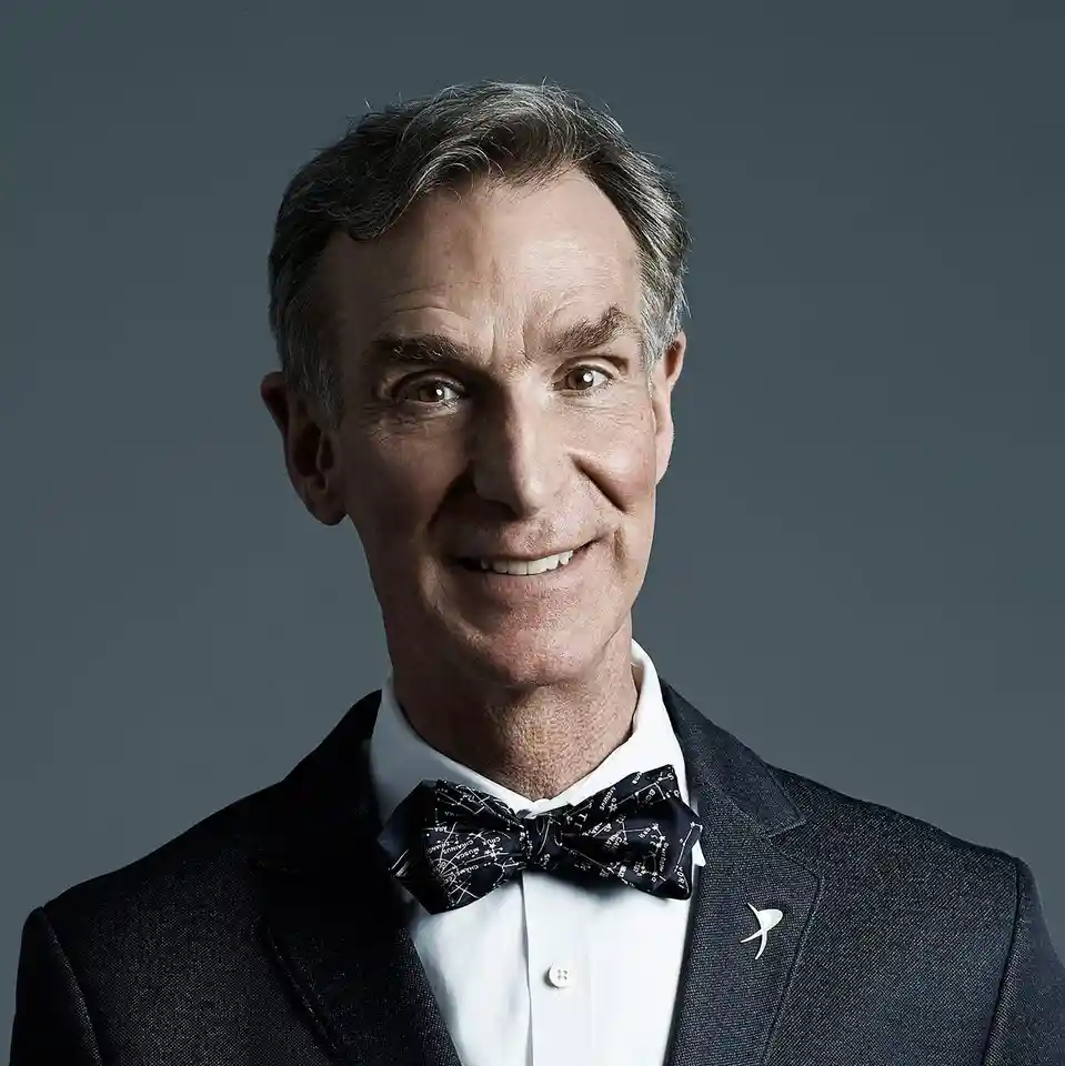 A professionally shot portrait of a middle-aged man with graying hair, wearing a dark suit, white shirt, and a bow tie…