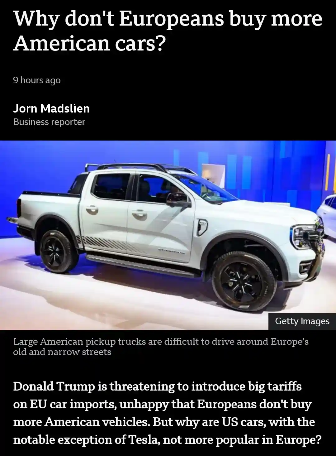 The image shows a white American pickup truck, likely a Ford F-150, displayed at an auto show with a blue background…