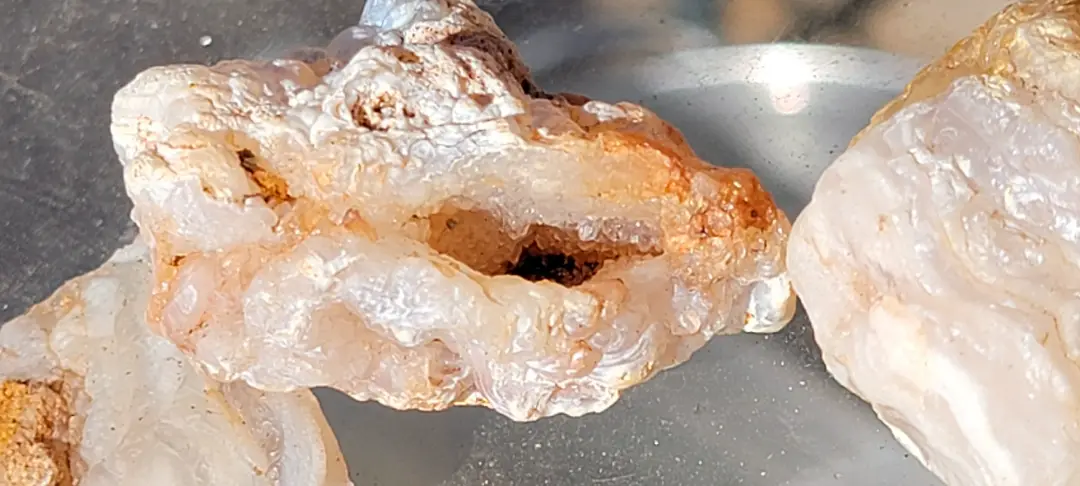 a close-up photo of a geode with a rough, crystalline exterior and a hollow interior, sitting on a metallic surface next to…