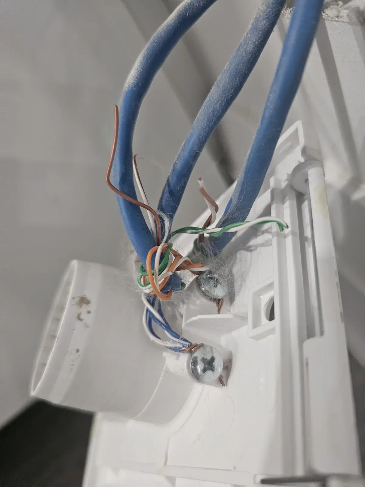 A close-up photo shows a messy, dusty electrical junction box with blue cables and exposed copper wires tangled together…