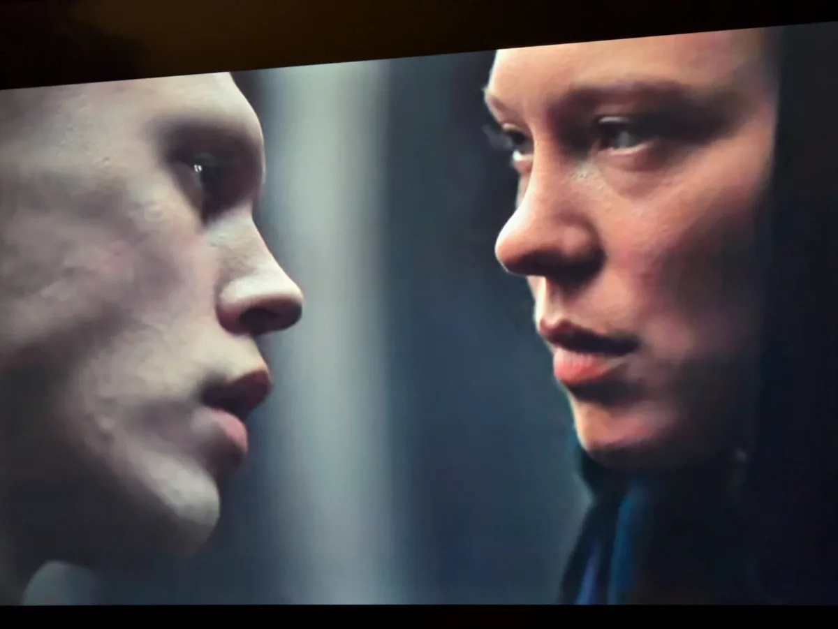A close-up shot shows two people facing each other in profile, their noses nearly touching, with intense, serious…