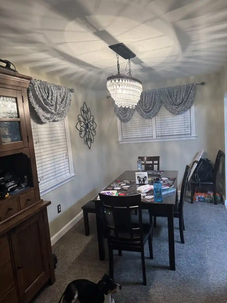 A dining room with a crystal chandelier hanging from a ceiling that has been visibly distorted into a wavy, uneven shape…