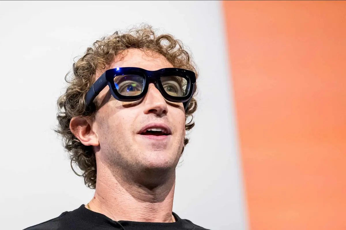 a close-up photo of mark zuckerberg wearing large, futuristic-looking smart glasses with a black frame and visible tech…